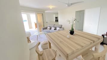 A modern living room with a large wooden dining table, two wooden chairs, a grey sofa, and a ceiling fan.