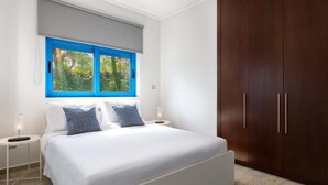 Ein Schlafzimmer mit einem Bett, zwei Nachttischen, einem Fenster mit blauen Rahmen und einem Holzschrank.