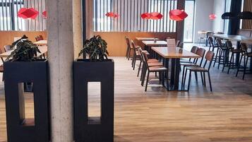 Un restaurante moderno con suelo de madera, mesas negras y de madera, y decoraciones rojas colgantes.