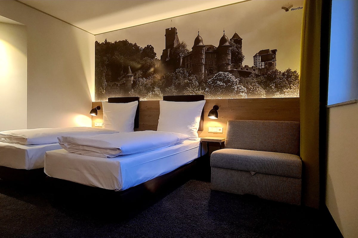 A hotel room with two beds, a chair, and a large wall mural of a castle.