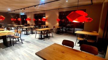 Un interior de restaurante moderno con mesas y sillas de madera, iluminación colgante roja y suelo de madera.