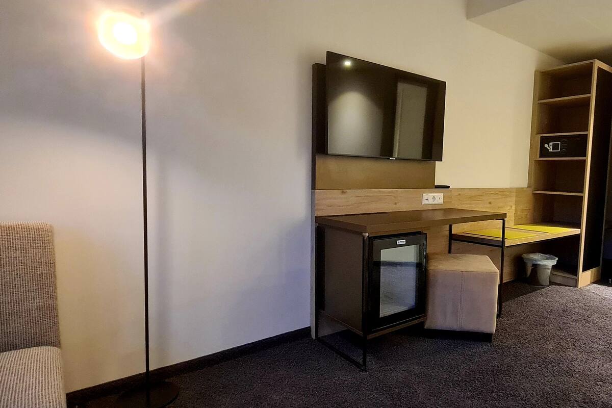 A compact hotel room with a bed, a small desk, a mirror, and a TV.
