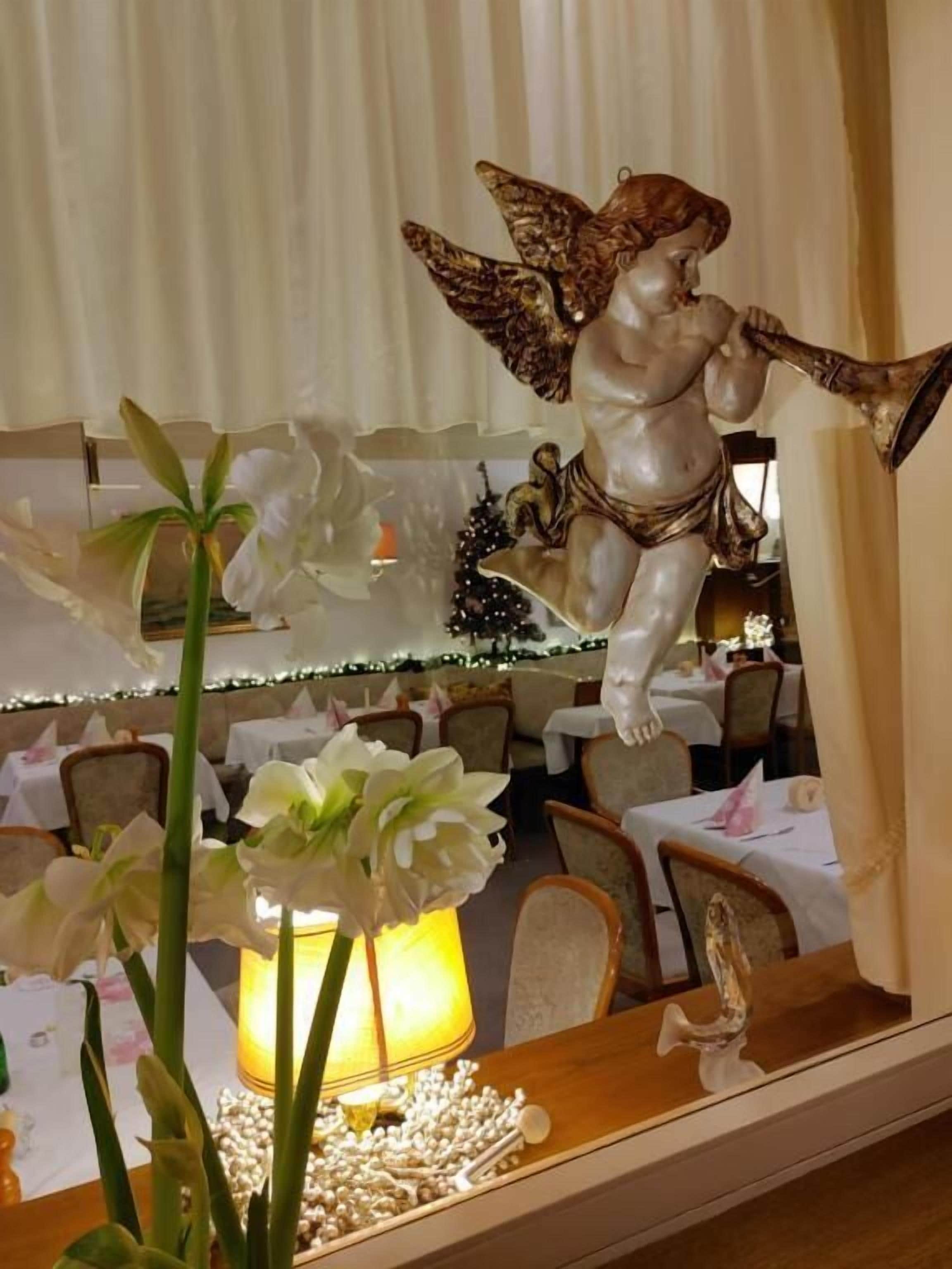 A dining area with a table set for two, a decorative angel figurine, and a vase with white flowers.