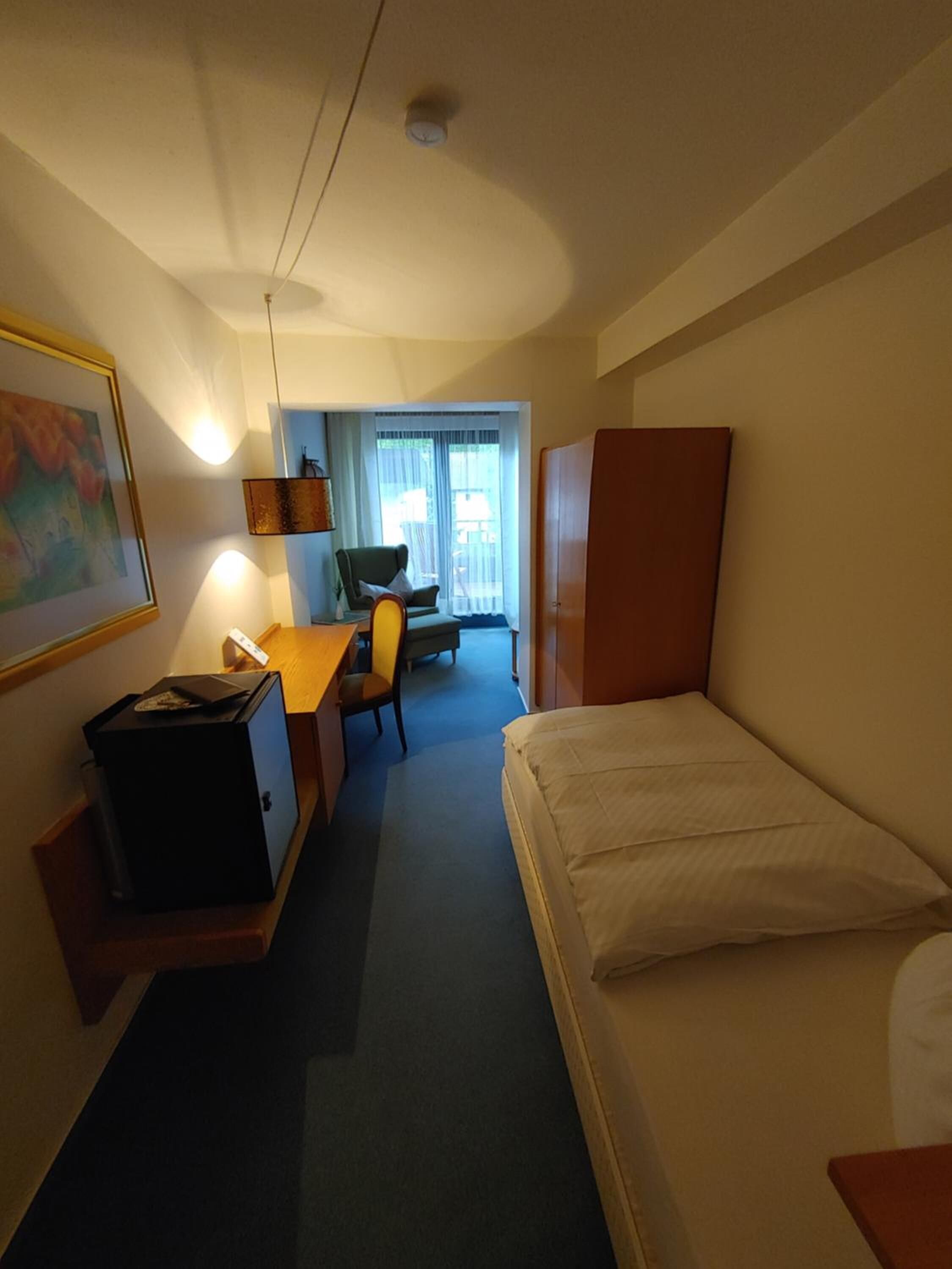 A hotel room with a bed, desk, chair, and a small cabinet.
