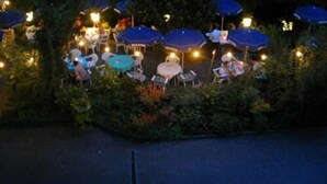 An outdoor seating area with tables and chairs under blue umbrellas, surrounded by greenery. - Hotel Adler (Lichtenstein)
