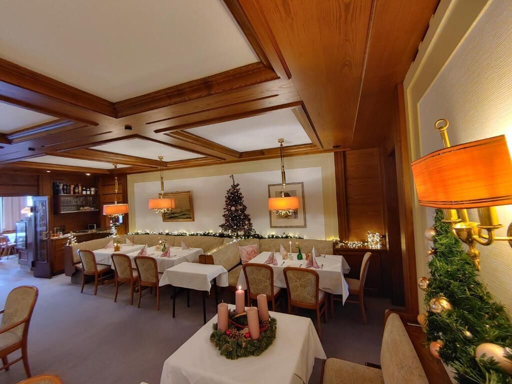 Een eetruimte met gedekte tafels, een kerstboom en wandlampen.