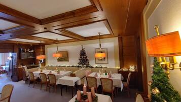 Een eetruimte met gedekte tafels, een kerstboom en wandlampen.