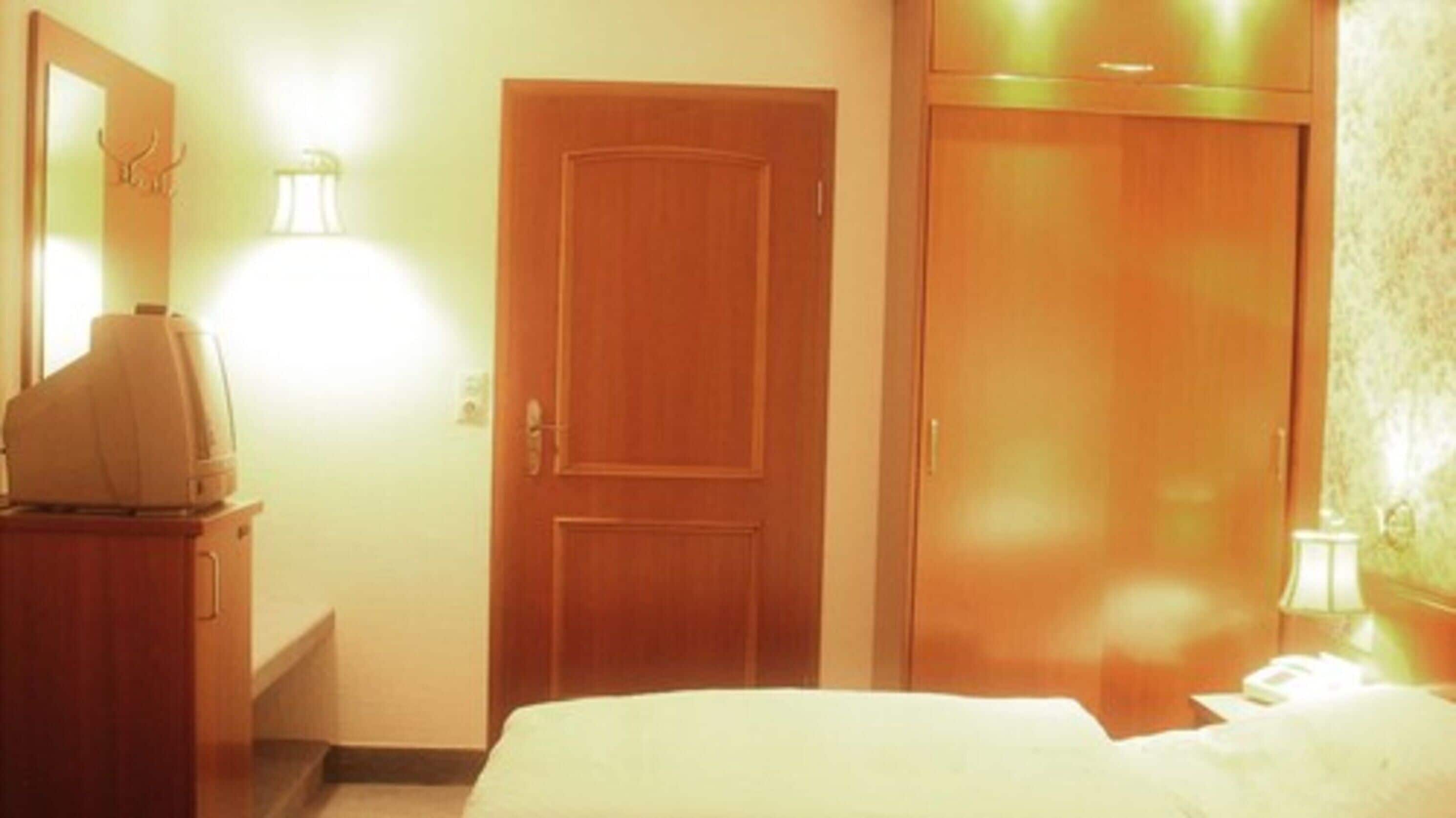 Hotellihuone, jossa on sänky, puinen vaatekaappi ja televisio puisen lipaston päällä.