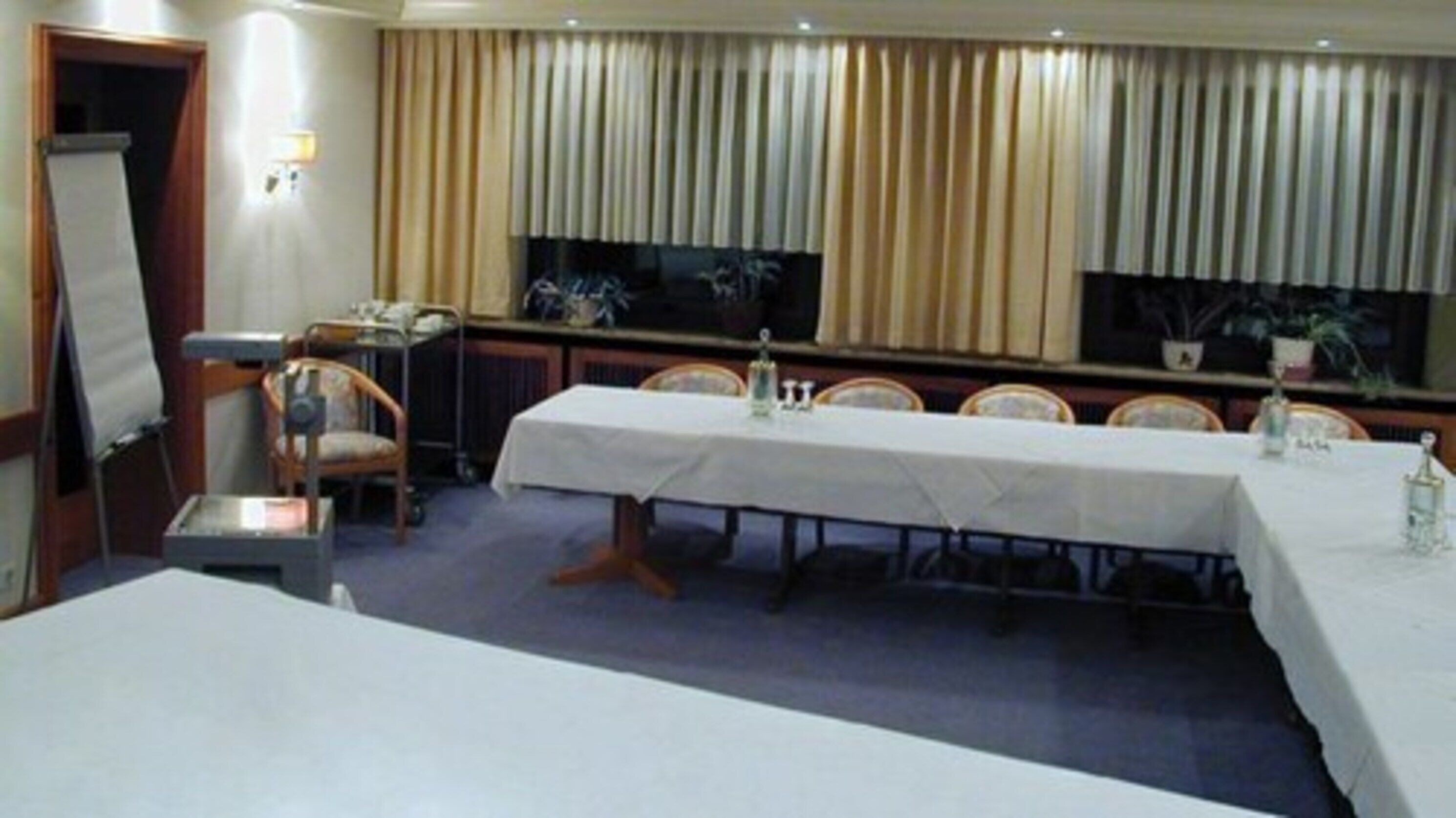 Un salón de conferencias con una larga mesa, sillas, un proyector y una ventana con cortinas.