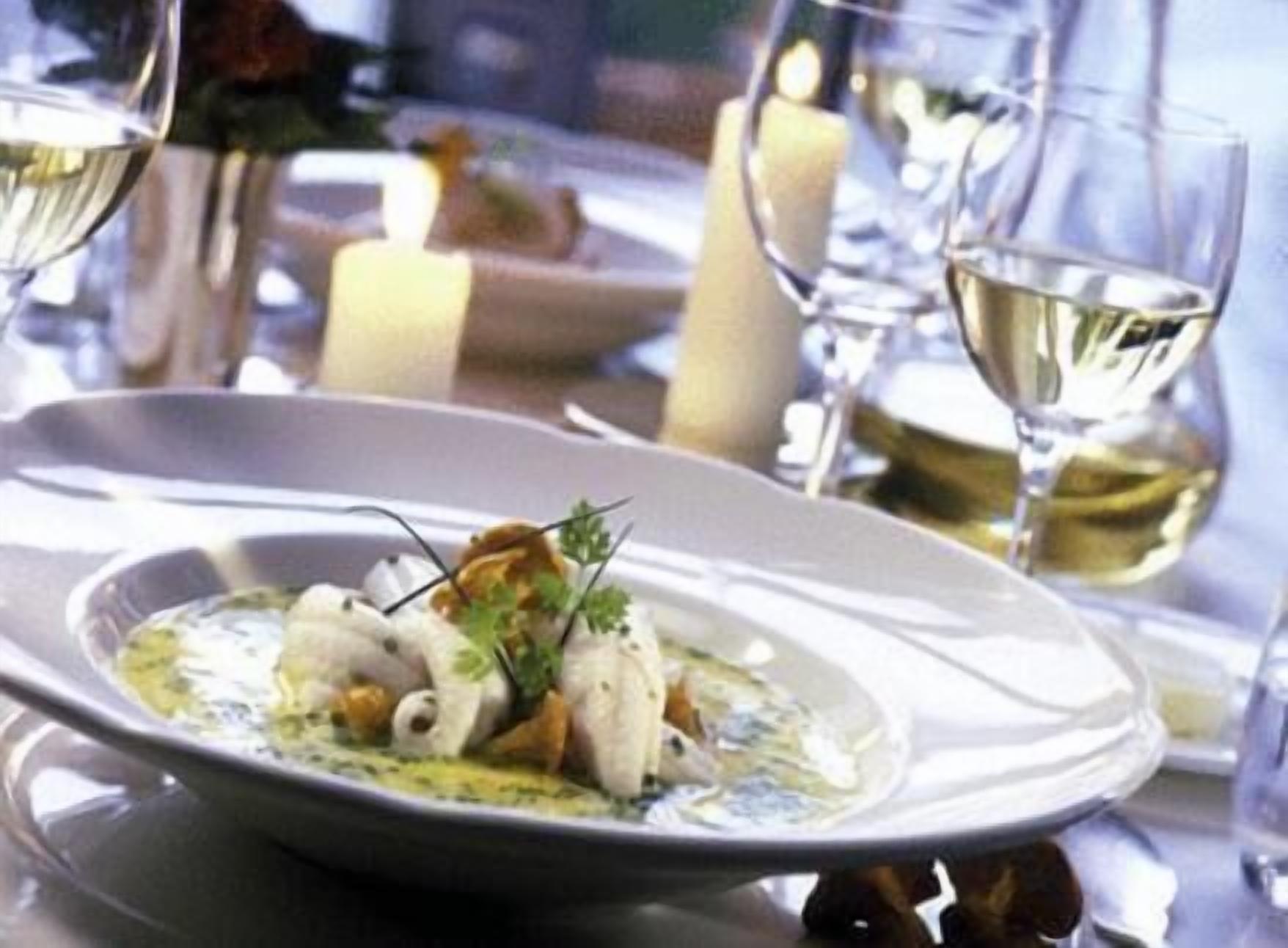 Een eettafel met een wit bord eten, een glas witte wijn en kaarsen.