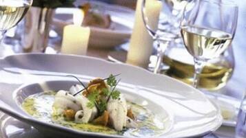 Een eettafel met een wit bord eten, een glas witte wijn en kaarsen.