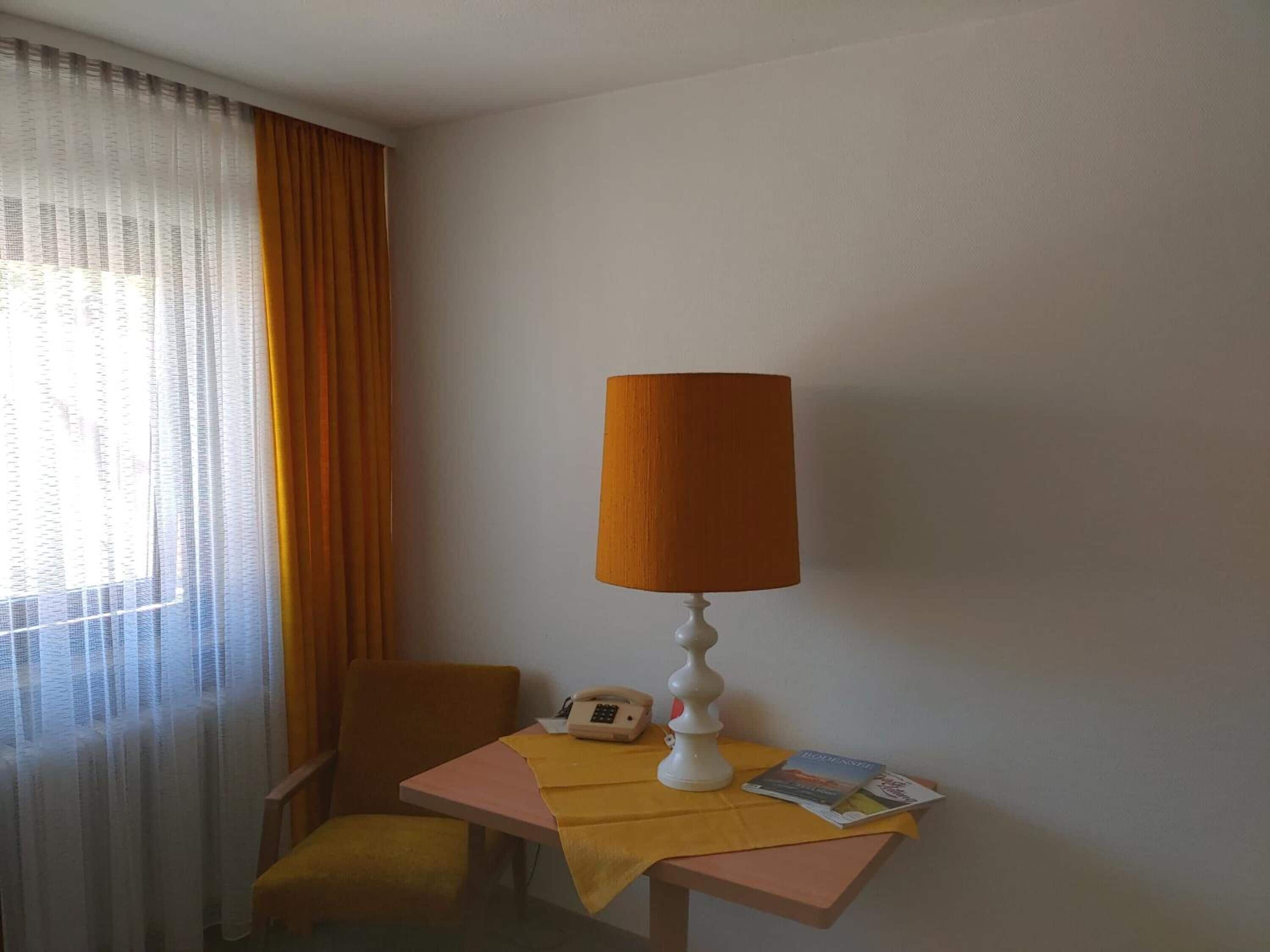 Habitación en esquina con una silla, una mesita, una lámpara, un teléfono y una revista.