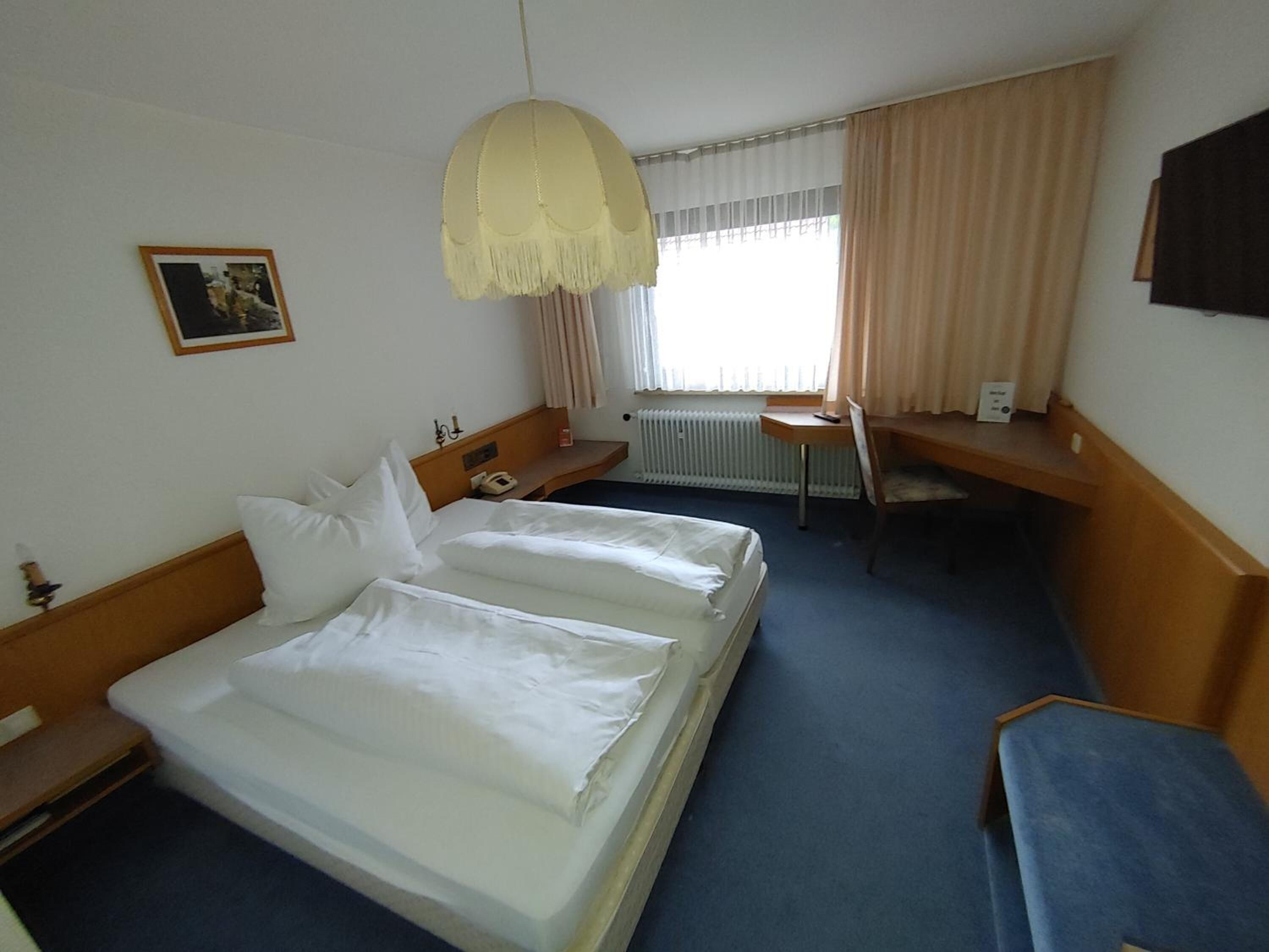 Una camera d'albergo con due letti, una scrivania, una sedia, un termosifone e una finestra con tende.