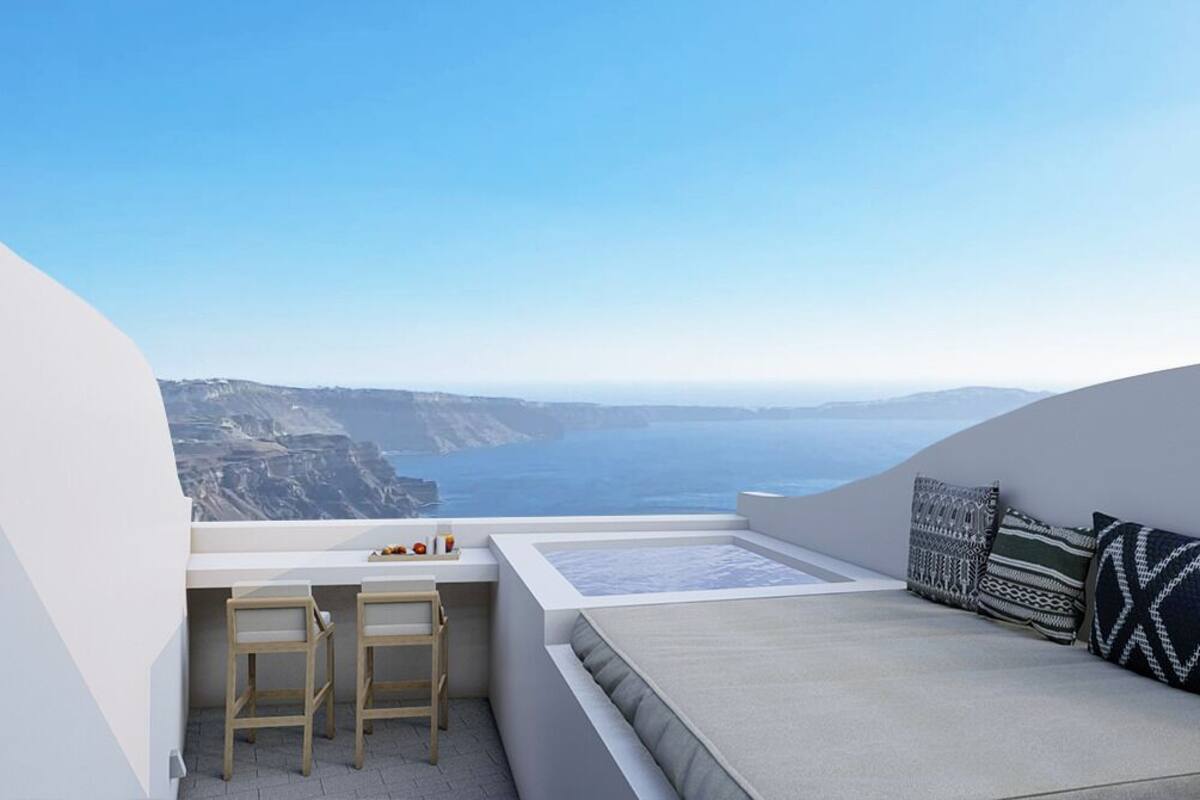 Un balcon moderne avec vue sur la mer, un coin salon avec des coussins et une petite table accompagnée d’une chaise.