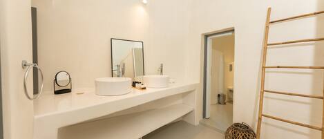 A modern bathroom with two sinks, a large mirror, and a wooden ladder.