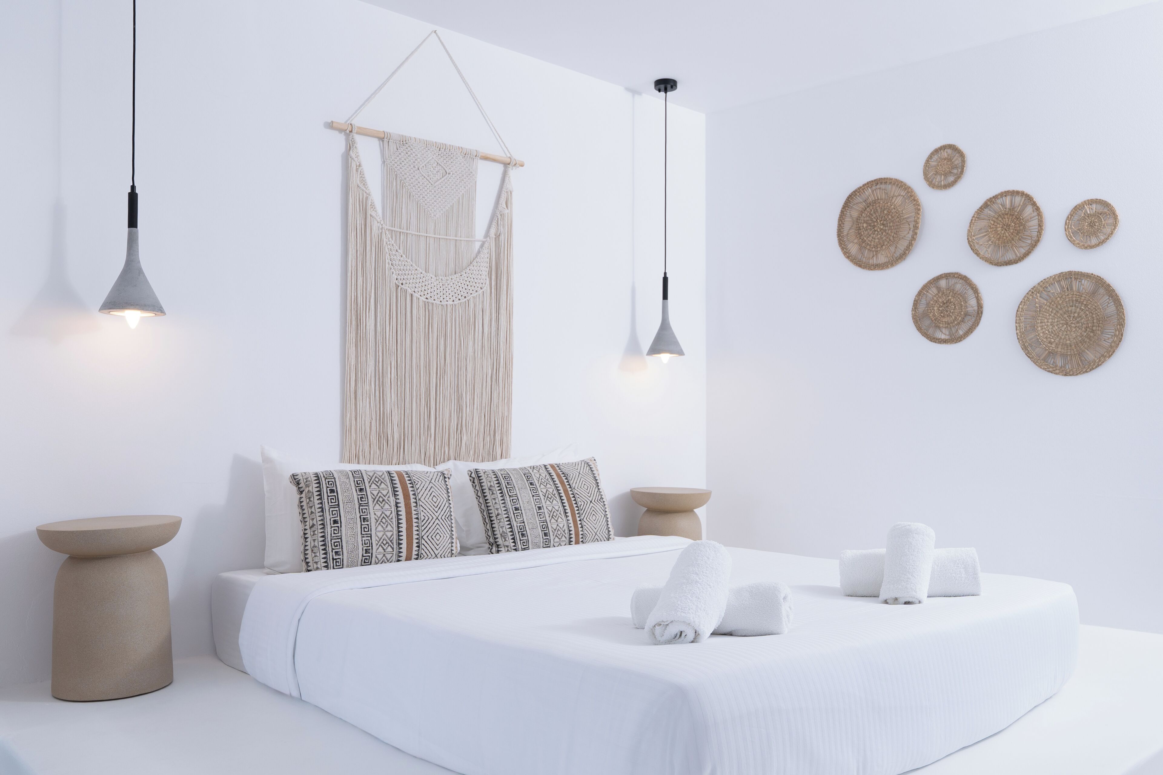 A minimalist bedroom with a bed, bedside tables, macrame wall hanging, pendant lights, and wall decor.