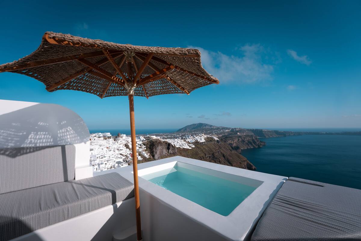 Une piscine à débordement située sur le toit, agrémentée d’un parasol en osier, offrant une vue sur une ville côtière et la mer.