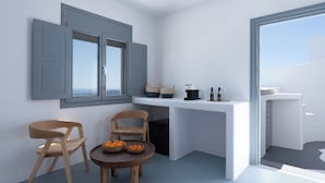Cocina compacta con comedor, que incluye una encimera blanca, dos sillas de madera, una mesita redonda con fruta y vistas a través de un ventanal grande.