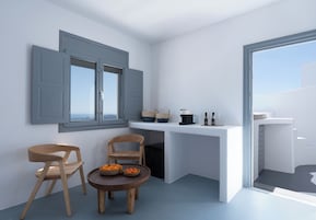 Cocina compacta con comedor, que incluye una encimera blanca, dos sillas de madera, una mesita redonda con fruta y vistas a través de un ventanal grande.