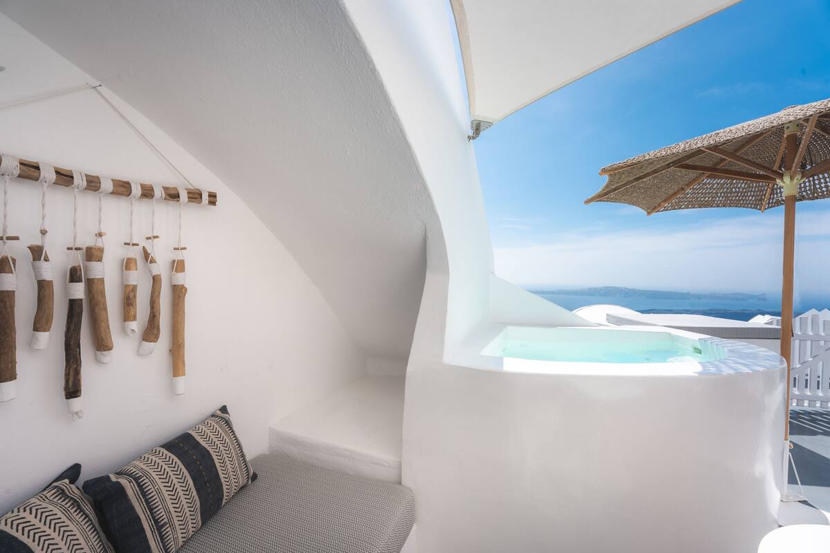 Un intérieur blanc avec un jacuzzi, une décoration en bois suspendue et une vue sur la mer.
