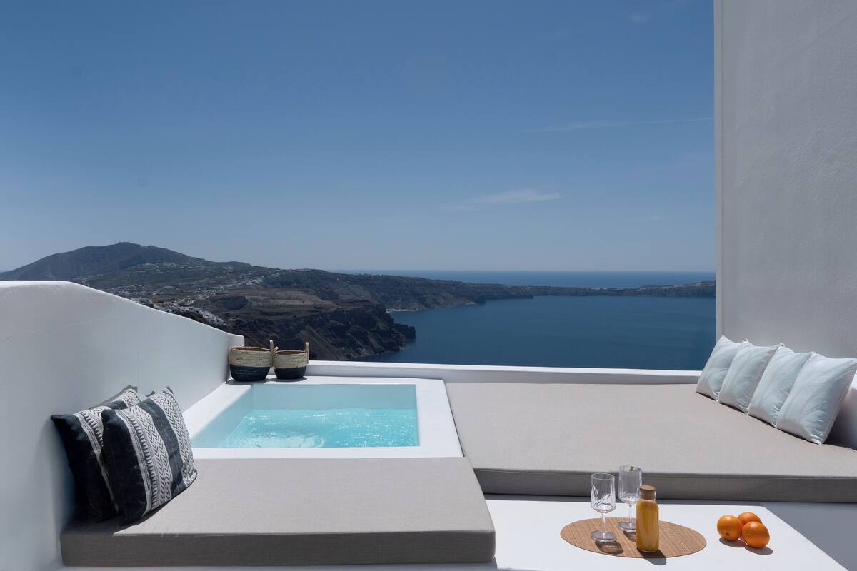 Un balcon avec vue sur la mer, un jacuzzi et une table avec des verres et des oranges.