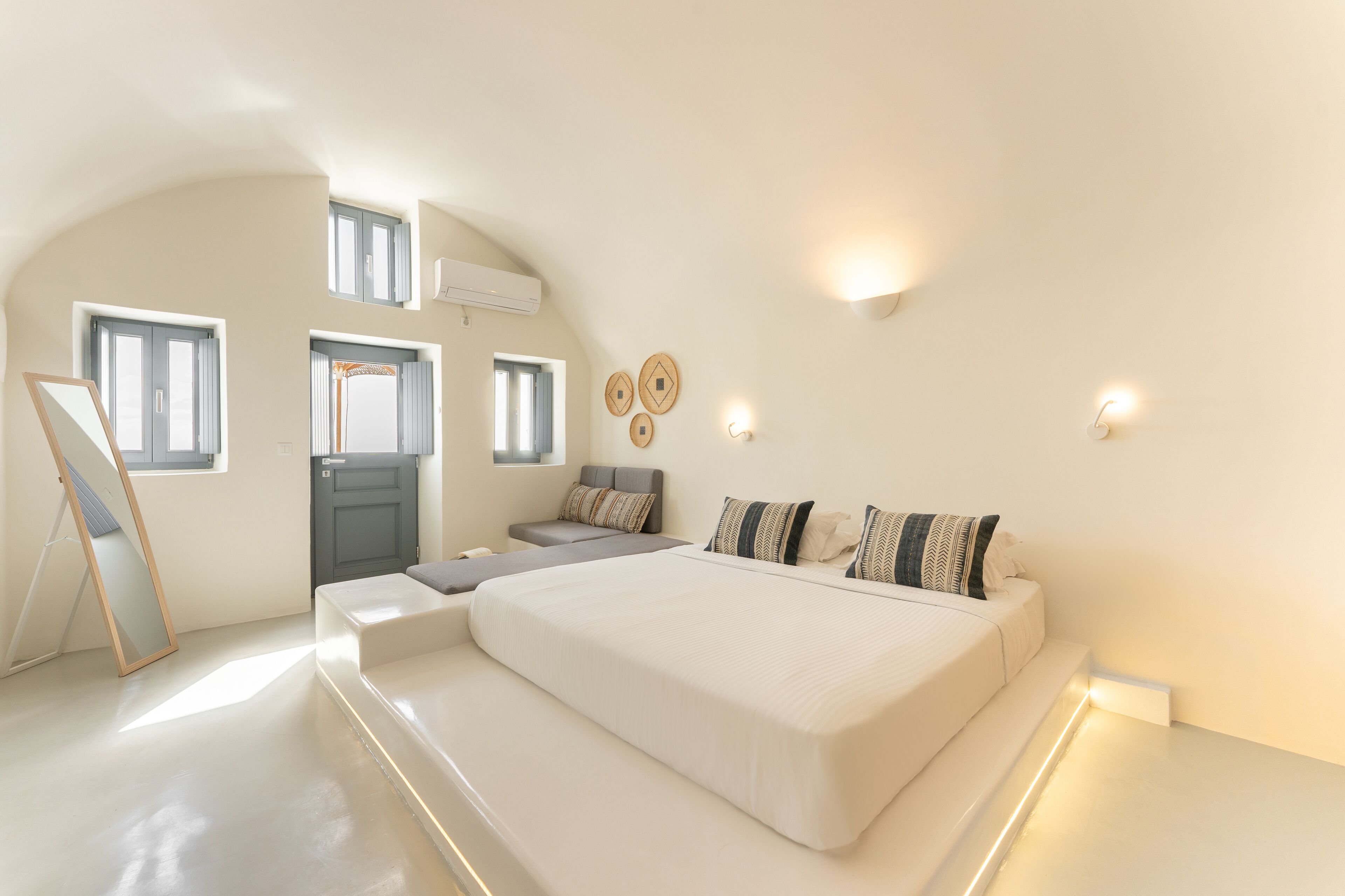 A modern bedroom with a large bed, a sofa, a desk, and a mirror.