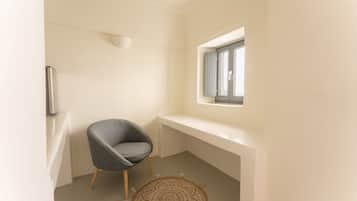 A small, modern room with a single gray chair, a round patterned rug, and a window with blinds.