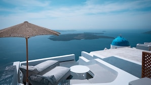 Habitación de hotel frente al mar, con vista al océano, una cúpula azul y muebles blancos.