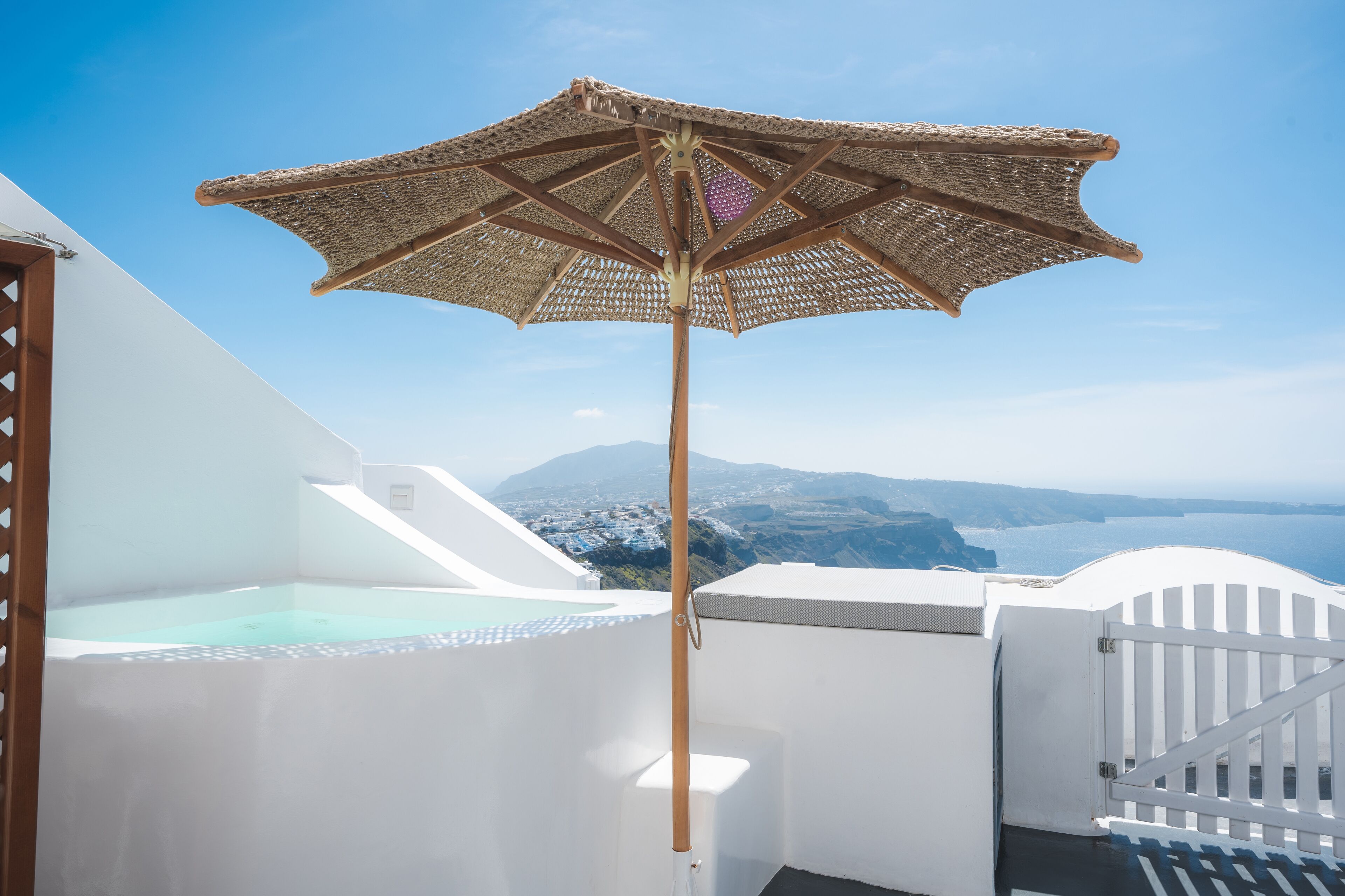 Un edificio bianco con un grande ombrellone, una piscina e vista sulla costa.