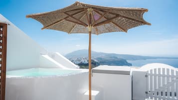 A white building with a large woven umbrella, a pool, and a view of the coastline.