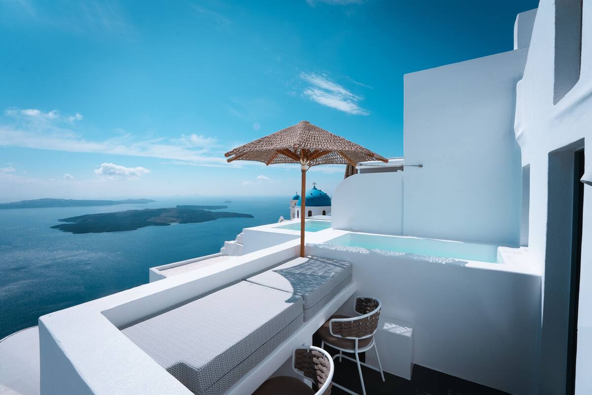 Un balcon avec vue sur la mer, un bâtiment blanc et un parasol en osier.