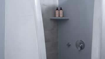 Ein Badezimmer mit Duschabtrennung, einem Ablagebereich mit zwei Flaschen und einem Wasserhahn.