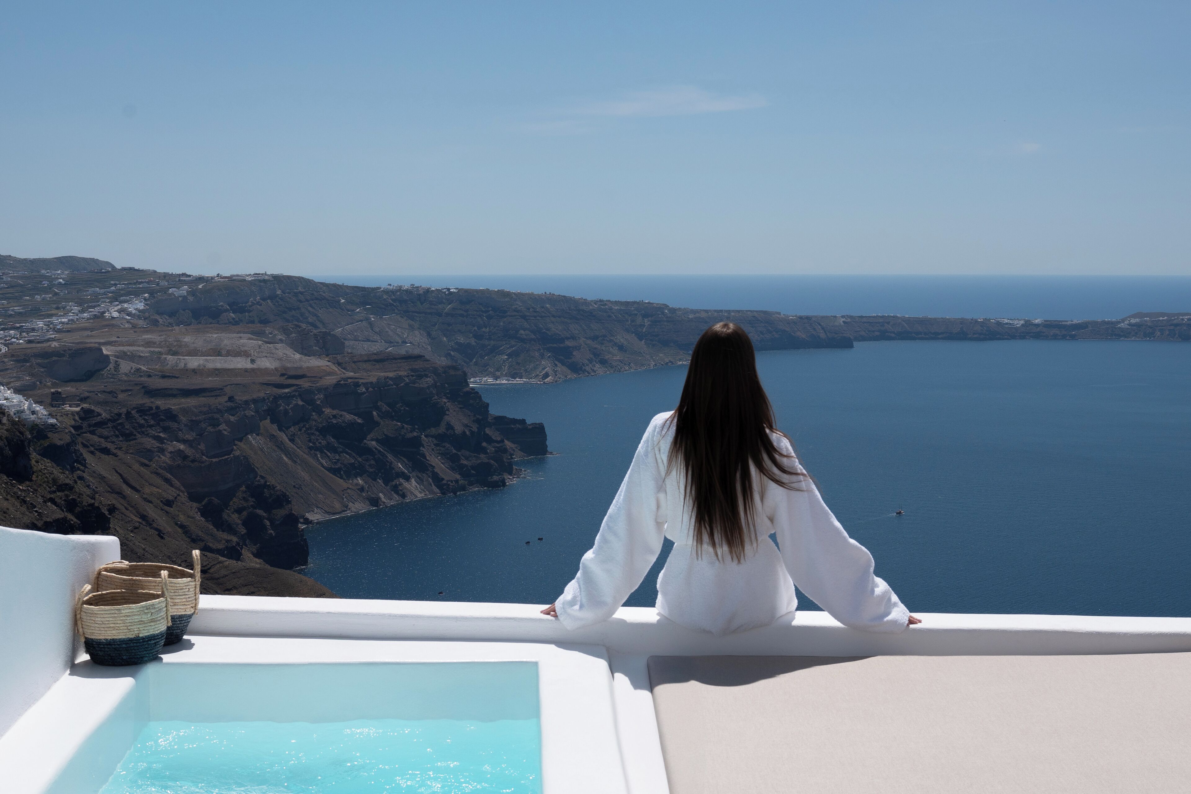A person sitting by a pool with a view of cliffs and the sea.