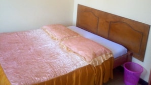 A small, neatly made bed with a wooden headboard, a yellow bedspread, and a pink pillow. There is a wooden hanger on the wall and a purple laundry basket on the floor. - Kikuyu Guest House (Kikuyu)