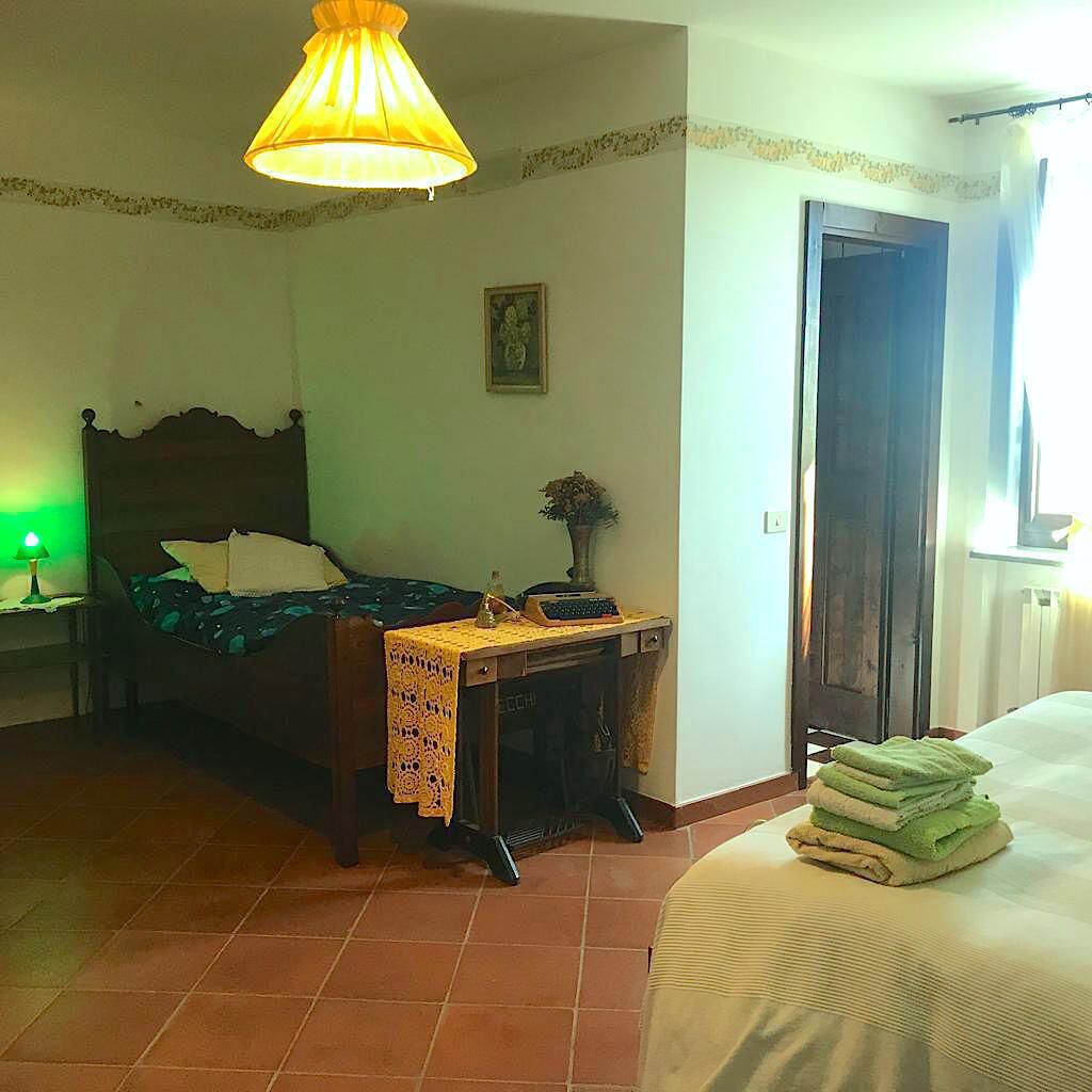 A bedroom with a bed, a desk with a lamp, a chair, a door, and a window.
