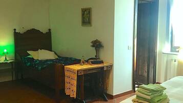 A bedroom with a bed, a desk with a lamp, a chair, a door, and a window.