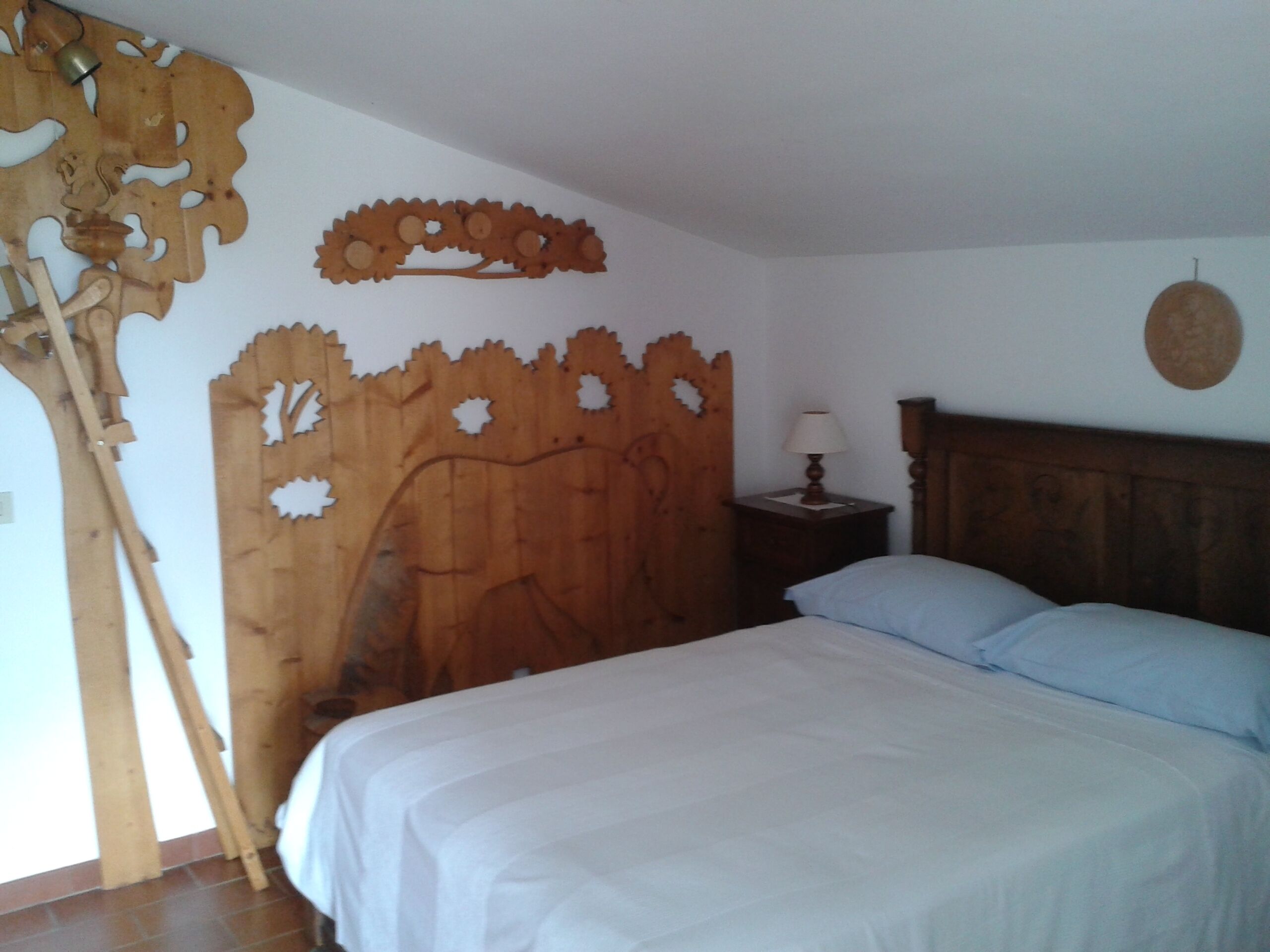 Una camera da letto con una testiera in legno, un letto con biancheria bianca, un comodino con una lampada e una sveglia a muro.