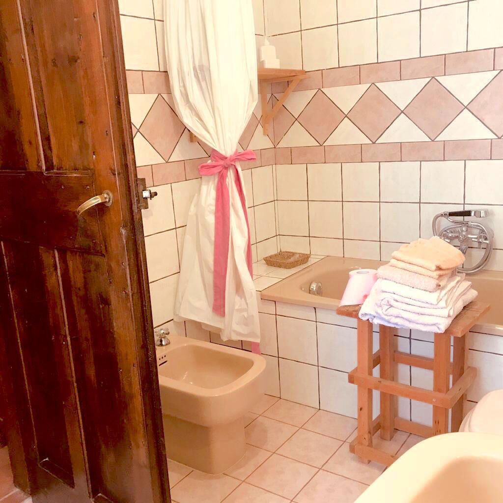 Ein Badezimmer mit Holztür, einem Bidet, einer Badewanne und einem hölzernen Hocker mit Handtüchern.