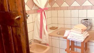 Ein Badezimmer mit Holztür, einem Bidet, einer Badewanne und einem hölzernen Hocker mit Handtüchern.