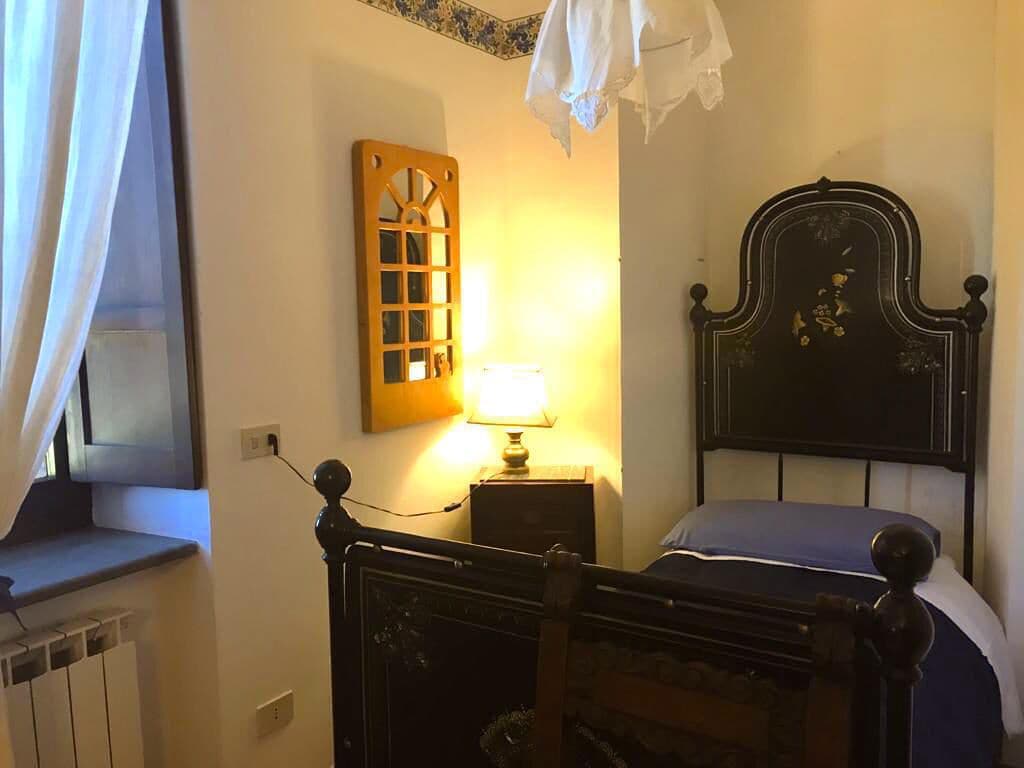 Ein Schlafzimmer mit einem hölzernen Bett, einem Nachttisch mit Lampe, einem Fenster mit Vorhängen und einer an der Wand befestigten Holzvertäfelung.