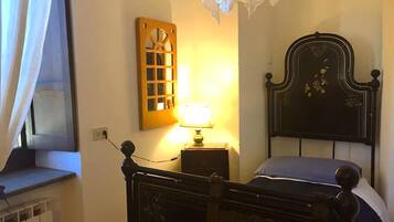 Ein Schlafzimmer mit einem hölzernen Bett, einem Nachttisch mit Lampe, einem Fenster mit Vorhängen und einer an der Wand befestigten Holzvertäfelung.