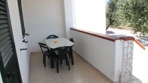 Een klein balkon met een tafel en stoelen, een stenen muur en uitzicht op bomen.