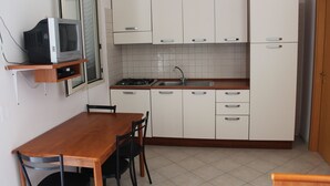 Een kleine keuken met witte kasten, een houten tafel en een ingebouwde televisie.