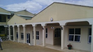 A building with a series of arched doorways and windows, a paved walkway, and a trash bin.