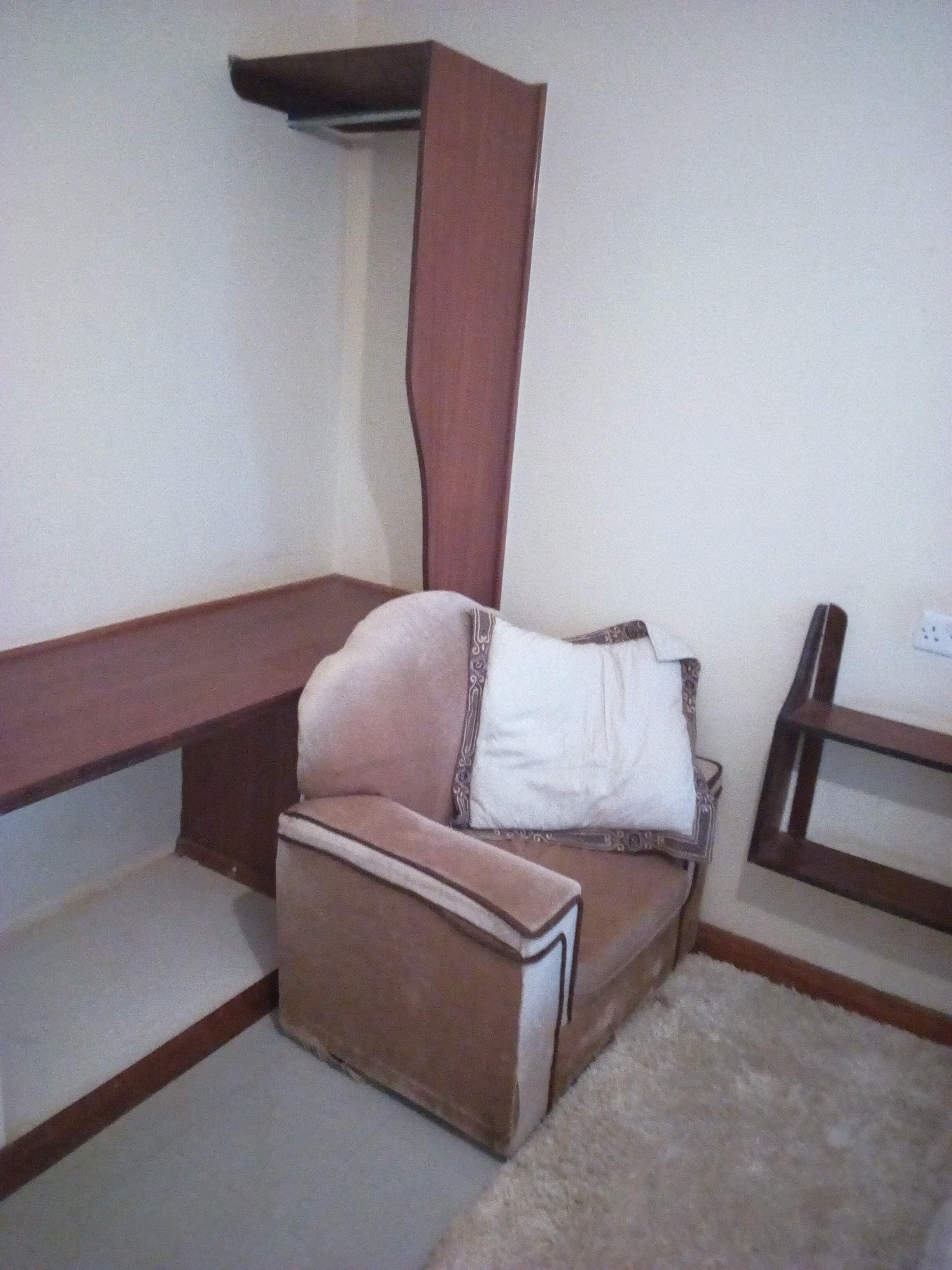 A corner room with a brown sofa, a white pillow, and a wooden side table.