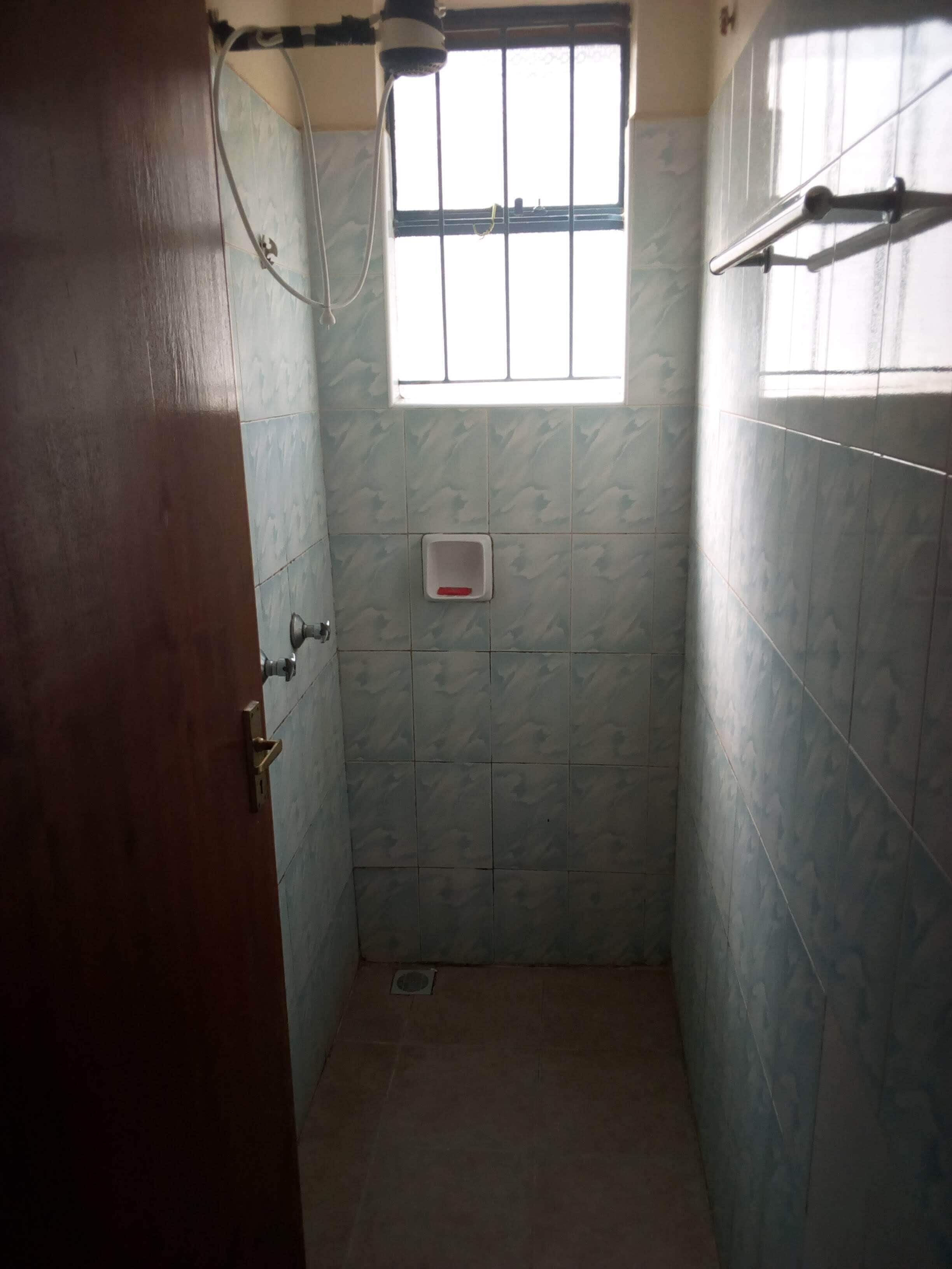 Une petite salle de bain carrelée, avec une fenêtre, une pomme de douche et des toilettes.