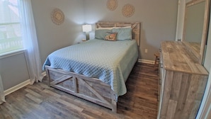 Een slaapkamer met een bed, een houten hoofdbord, een plafondventilator, een nachtkastje met een lamp en een dressingkast.