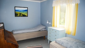 A bedroom with a bed, a bedside table, a lamp, a dresser, and a window with curtains.