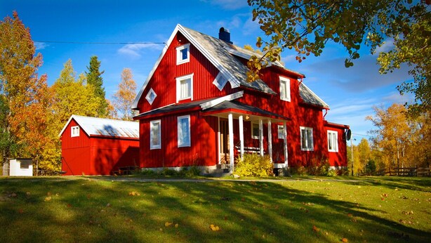 A red barn with a white roof, surrounded by trees with autumn foliage.