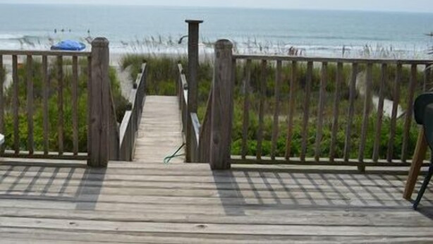 A wooden boardwalk leading to a beach with a view of the ocean.